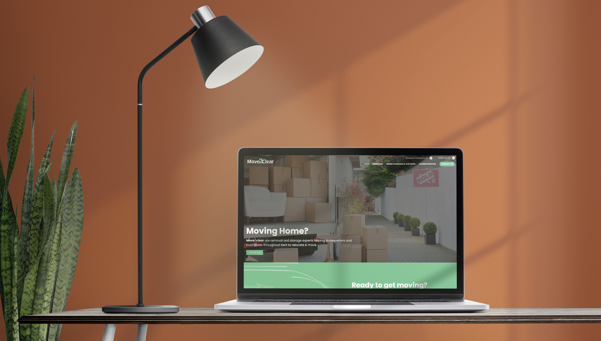 A web design shown on a laptop with a lamp and plant against an orange background